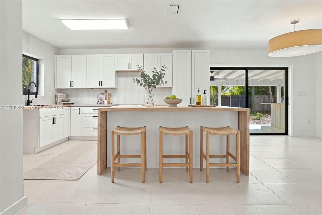 Kitchen featuring white Shaker-style cabinetry, a central island with wood-finished waterfall edge, tile flooring, and black-framed sliding glass doors