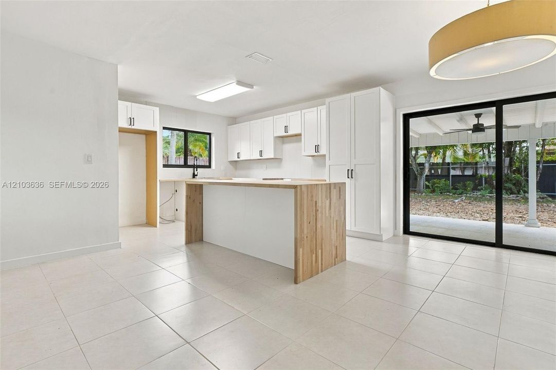 Kitchen featuring white cabinetry, wood-surface center island, light-toned tile flooring, and oversized sliding glass doors