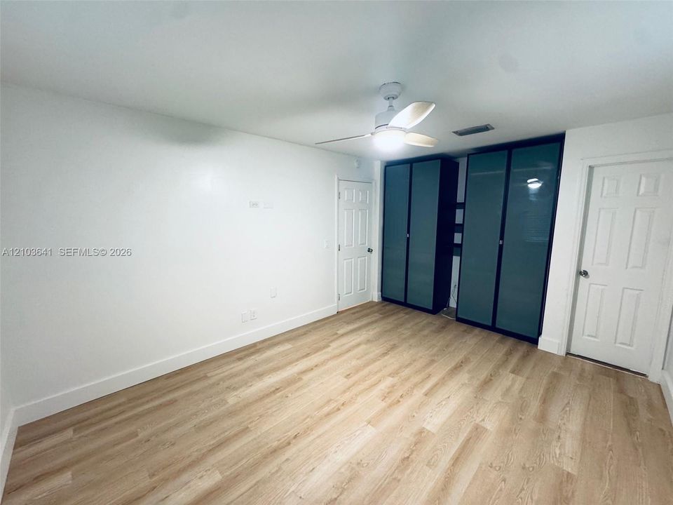Wood-finish flooring, white walls, built-in cabinetry with frosted glass panels, and a ceiling-mounted light fixture with fan