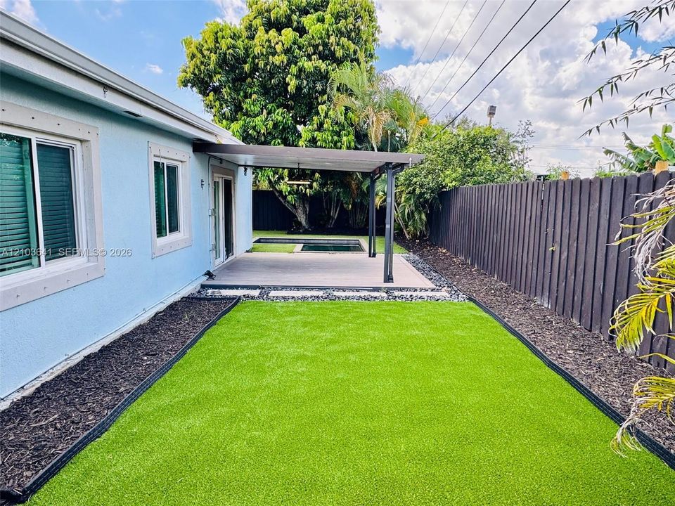 Rear exterior space featuring synthetic turf, covered concrete patio, built-in pool, and opaque privacy fencing