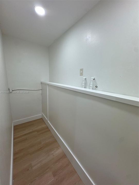 Utility area featuring wood-finish flooring, recessed ceiling lighting, and built-in plumbing connections with a mounted ledge