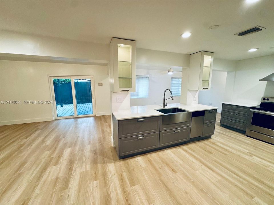Kitchen featuring gray cabinetry, stone-finish countertops, stainless steel farmhouse sink, glass-front upper cabinets, and wood-finish flooring