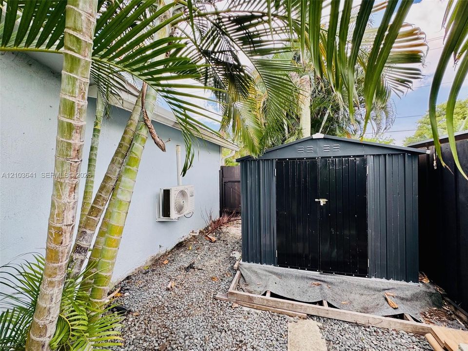 Exterior storage structure featuring metal construction and double-door entry situated on a stone-grounded area with privacy fencing and established palms