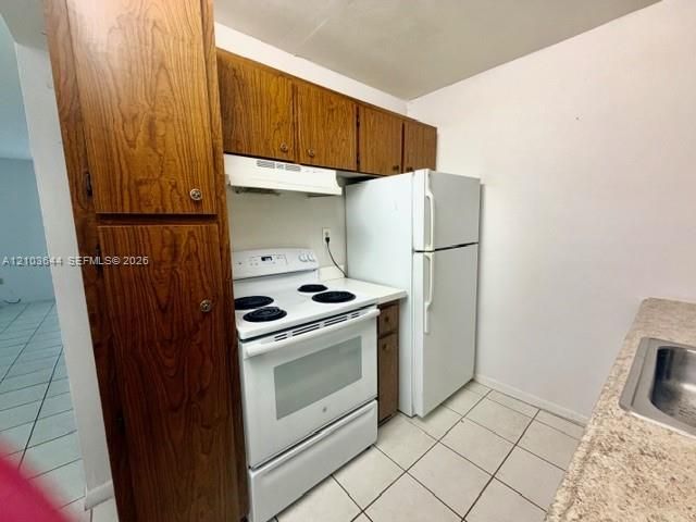 Kitchen featuring wood-finish cabinetry, white appliances, and tiled flooring