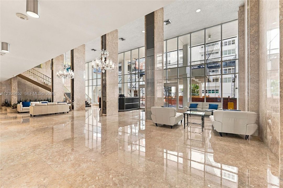 Expansive lobby featuring polished stone flooring, floor-to-ceiling glass walls, decorative chandeliers, and full-height stone-clad columns