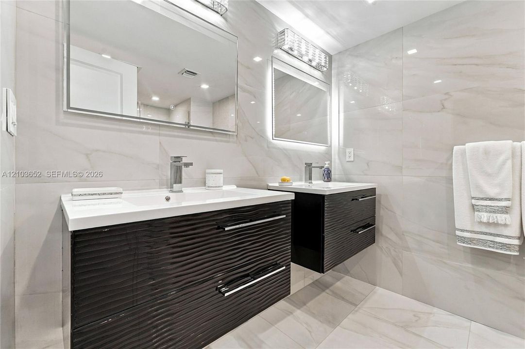 Dual floating vanities featuring dark-toned textured cabinetry, white integrated sinks, polished chrome fixtures, and full-wall porcelain tiling