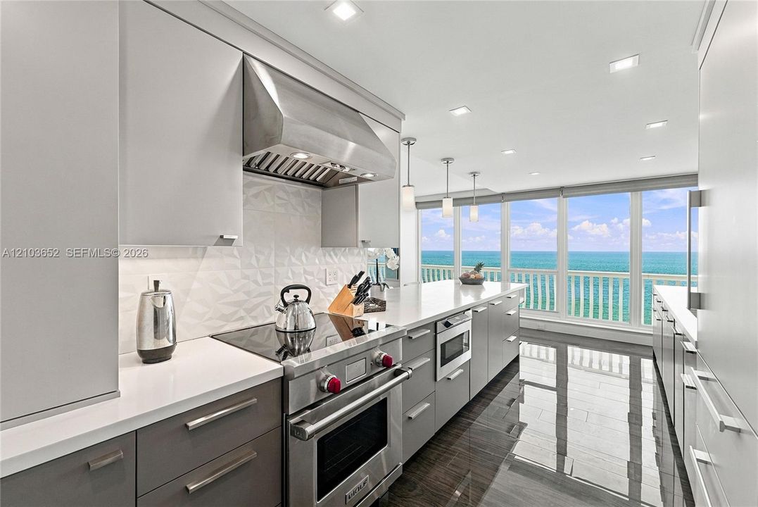 Modern kitchen featuring sleek two-tone cabinetry, professional-grade stainless steel range, geometric tile backsplash, stone countertops, and floor-to-ceiling windows with water exposure