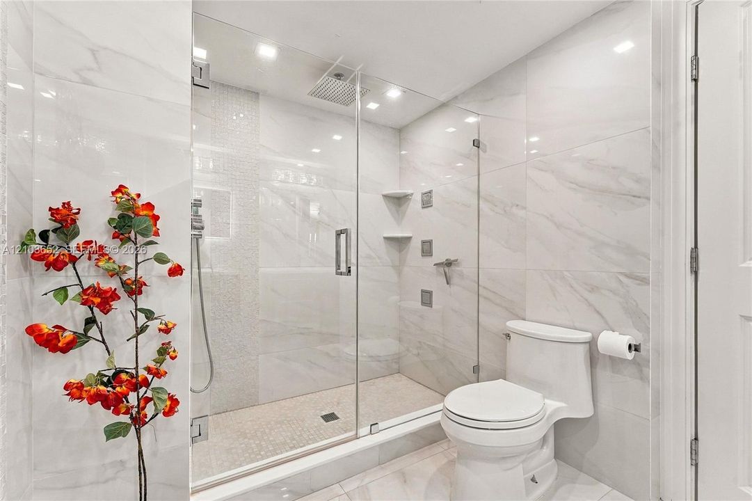 Walk-in shower featuring glass enclosure, ceiling-mounted rainfall showerhead, wall-mounted body sprays, built-in shelving, and floor-to-ceiling tile surround