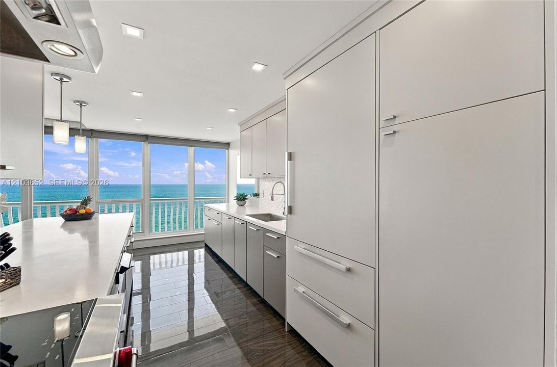 Kitchen featuring high-gloss cabinetry, stone countertops, integrated refrigerator, recessed lighting, and expansive windows with water backdrop