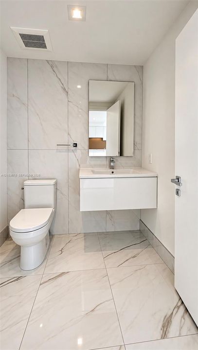 Floating vanity with a white integrated basin, floor-to-ceiling large-format tile wall, white stone-patterned floor tiling, rectangular mirror, and chrome single-handle faucet