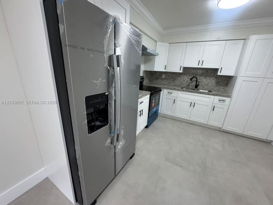 Kitchen featuring white shaker-style cabinetry, stainless steel refrigerator, stone-composite countertops, matte black hardware, and neutral ceramic tile flooring