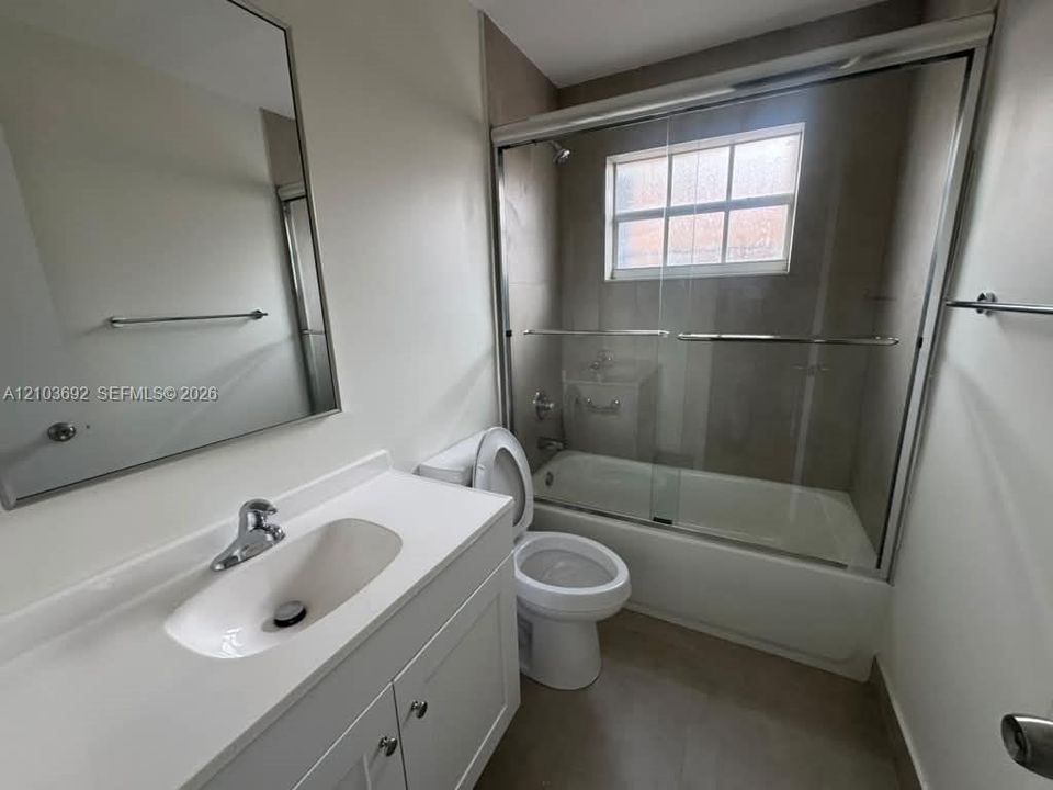 Bathroom featuring a white vanity with integrated sink, rectangular framed mirror, sliding glass shower enclosure, and a tub-shower combination