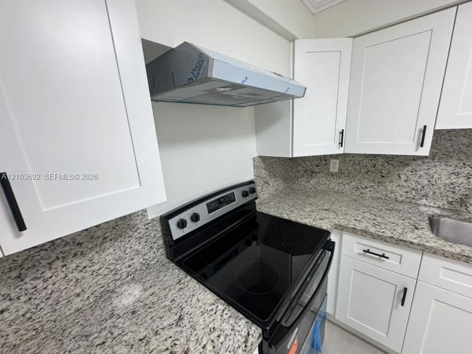 Kitchen featuring white Shaker-style cabinetry, stone-finish countertops, stainless steel range, and a mounted range hood with matte black hardware