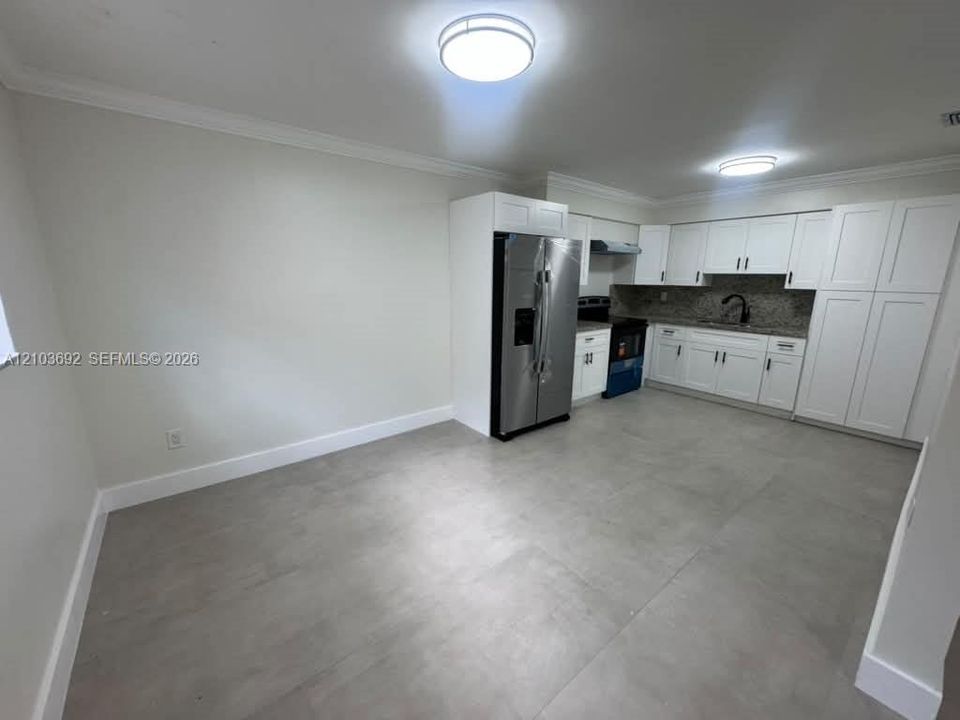 Kitchen featuring white shaker-style cabinetry, stainless steel side-by-side refrigerator, stone-composite countertops, matte black gooseneck faucet, and large-format tile flooring