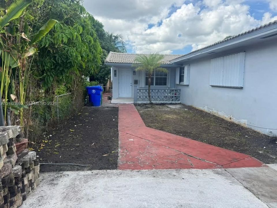 Single-story exterior featuring a light-toned facade, decorative concrete block entryway wall, metal hurricane shutters, and a concrete paver walkway