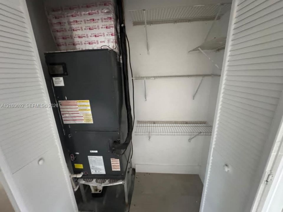 Utility closet featuring a mechanical unit and fixed wire shelving, enclosed by white louvered bi-fold doors