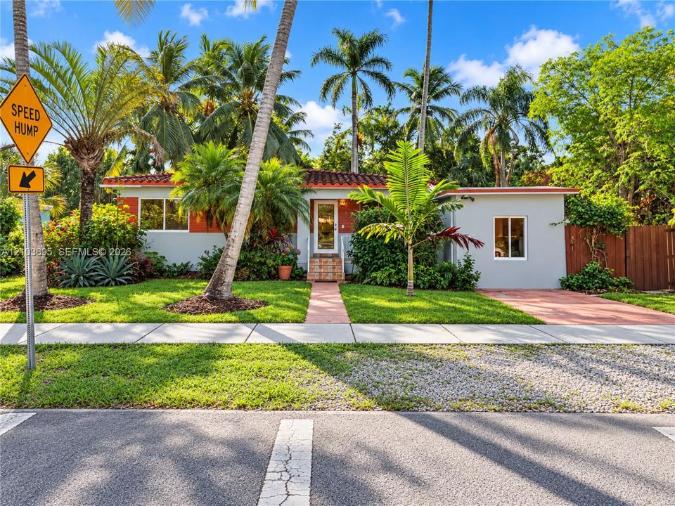 Single-story exterior featuring a clay tile roof, stucco finish, paved walkway, and mature landscaping
