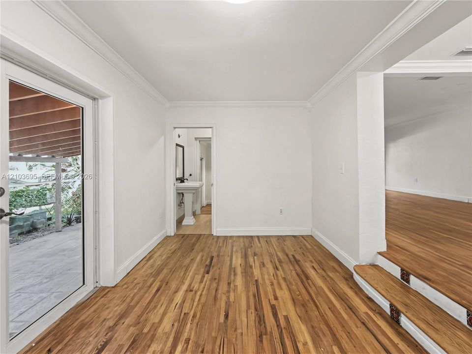 Wood-finish flooring, crown molding, glass-paned exterior door, and elevated platform featuring decorative tile accents