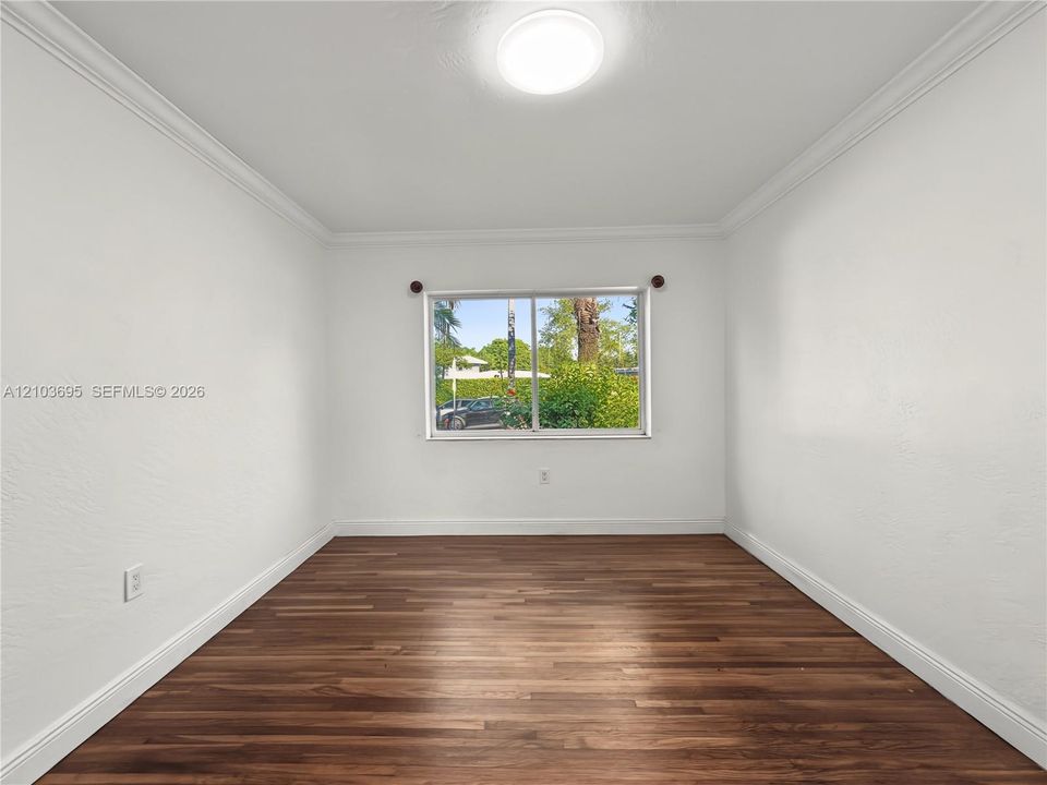 Interior space featuring wood-finish flooring, white walls, crown molding, and a dual-pane sliding window