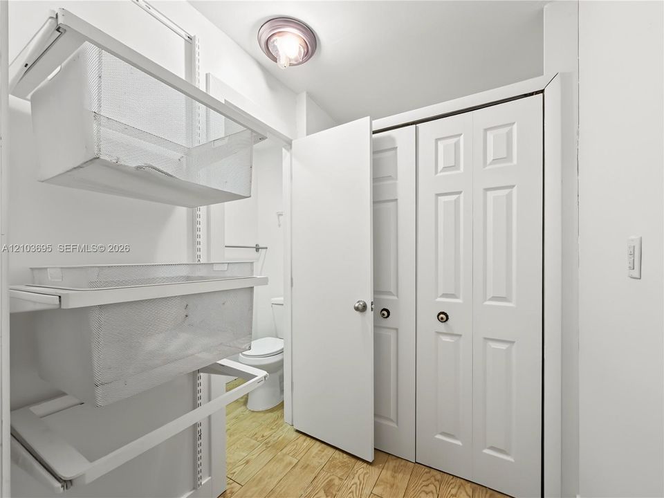 Wood-finish flooring, white paneled closet doors, and wall-mounted metal wire shelving system with flush-mount ceiling lighting