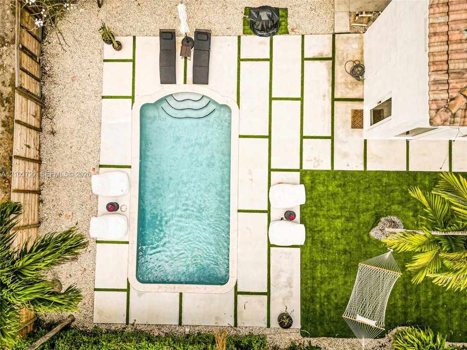 Rectangular swimming pool with built-in steps, light-colored paver decking with artificial turf accents, synthetic lawn area, and wood-style privacy fencing