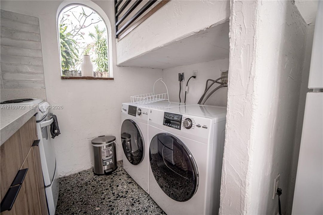 Laundry area featuring stone-aggregate flooring, arched window, wood-finish cabinetry, and solid-surface countertops