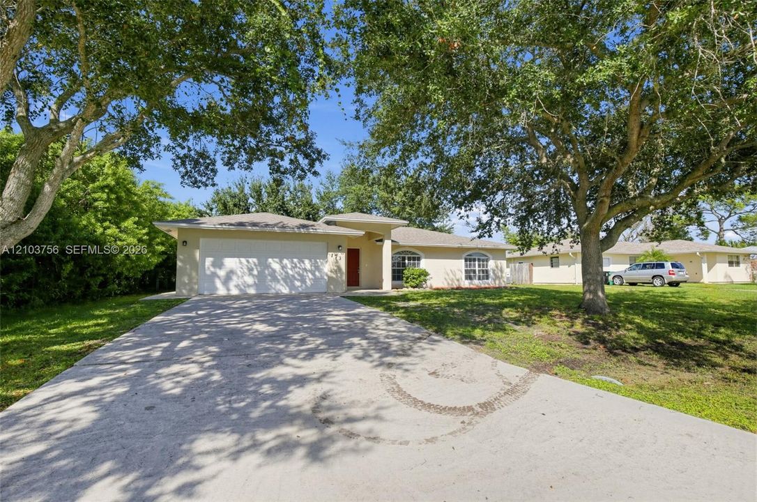 Single-story residence featuring a stucco exterior, an attached two-car garage, arched windows, and mature trees on a lot with lawn space