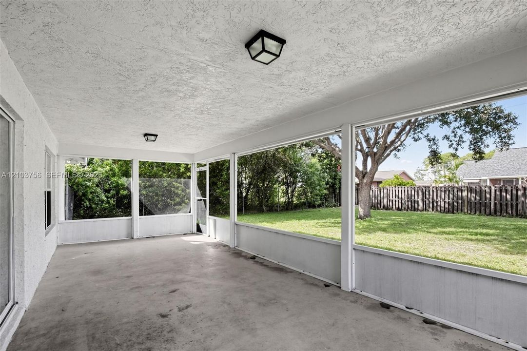 Screened-in patio featuring a concrete floor, textured ceiling, flush-mount lighting, and expansive window panels overlooking a fenced backyard