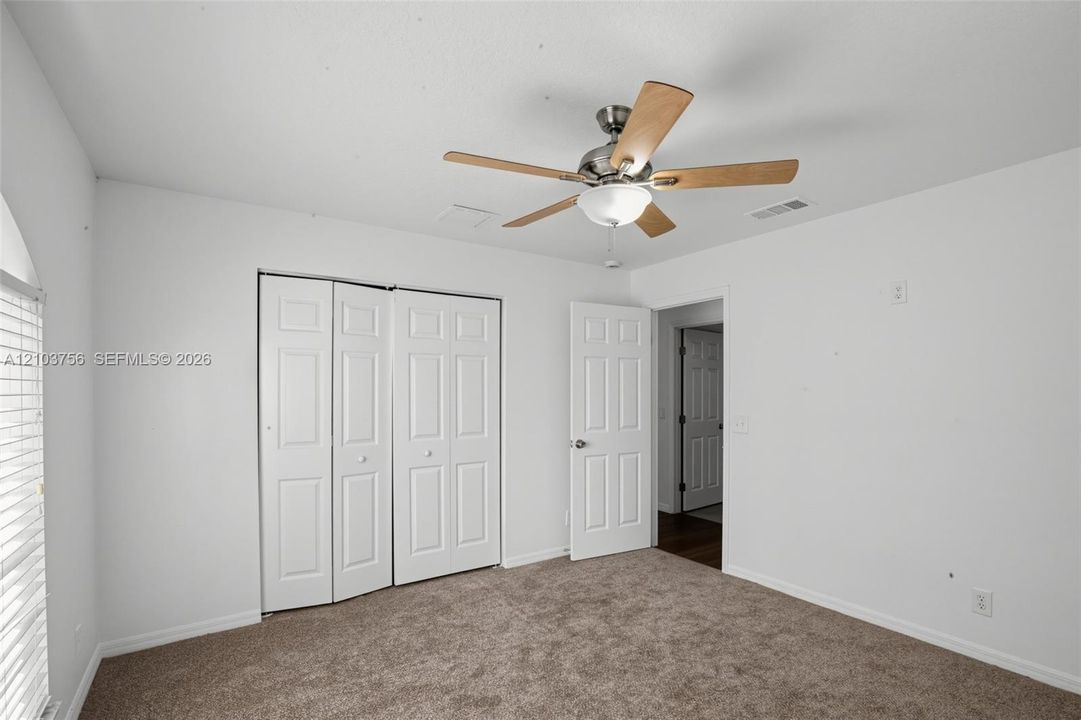 Neutral-toned carpeting, white walls, four-panel closet doors, and a ceiling fan with integrated lighting