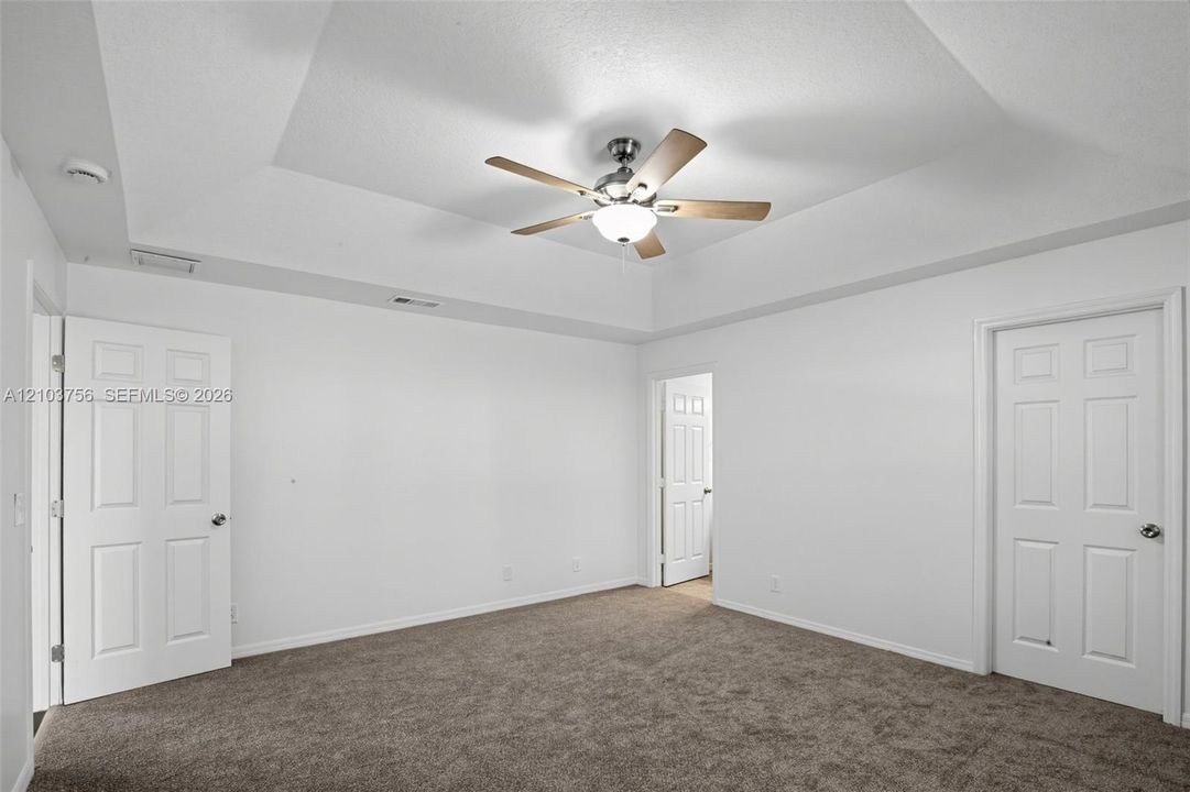 Tray ceiling with a multi-blade ceiling fan, neutral carpeting, and multi-panel interior doors