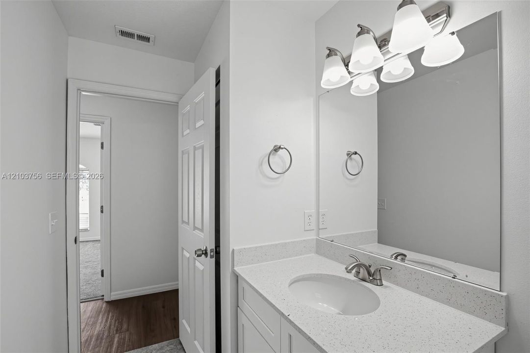 Bathroom vanity featuring a speckled white countertop, oval undermount sink, multi-light fixture, large wall-mounted mirror, and metal ring towel holder