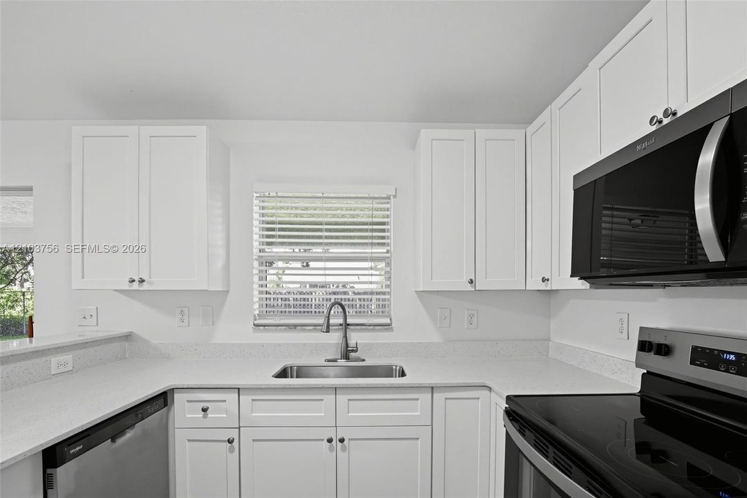 Kitchen featuring white shaker-style cabinetry, solid-surface countertops, undermount stainless steel sink with high-arc faucet, and stainless steel appliances
