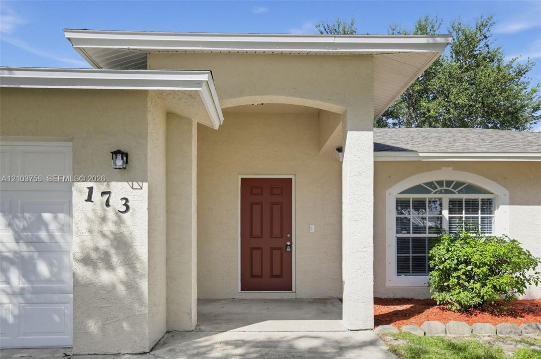 Single-story exterior featuring light-toned stucco siding, an attached two-car garage, an arched entryway, and multiple windows with decorative arched transoms