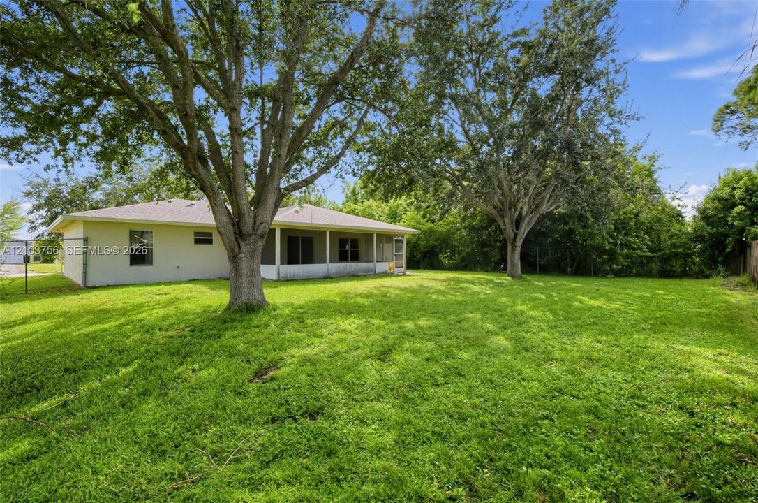 Spacious backyard featuring mature trees, a covered patio with screening, and light-colored stucco exterior siding