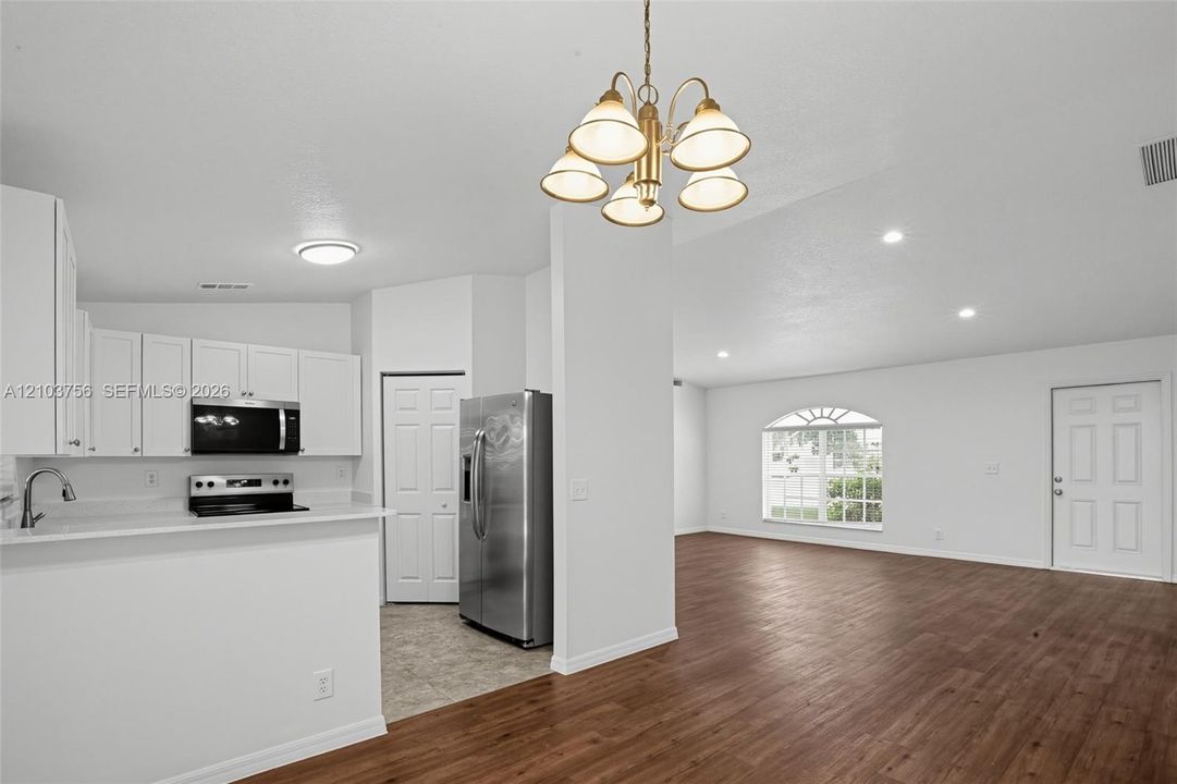 Kitchen featuring white cabinetry, wood-finish flooring, stainless steel appliances, and a multi-light chandelier