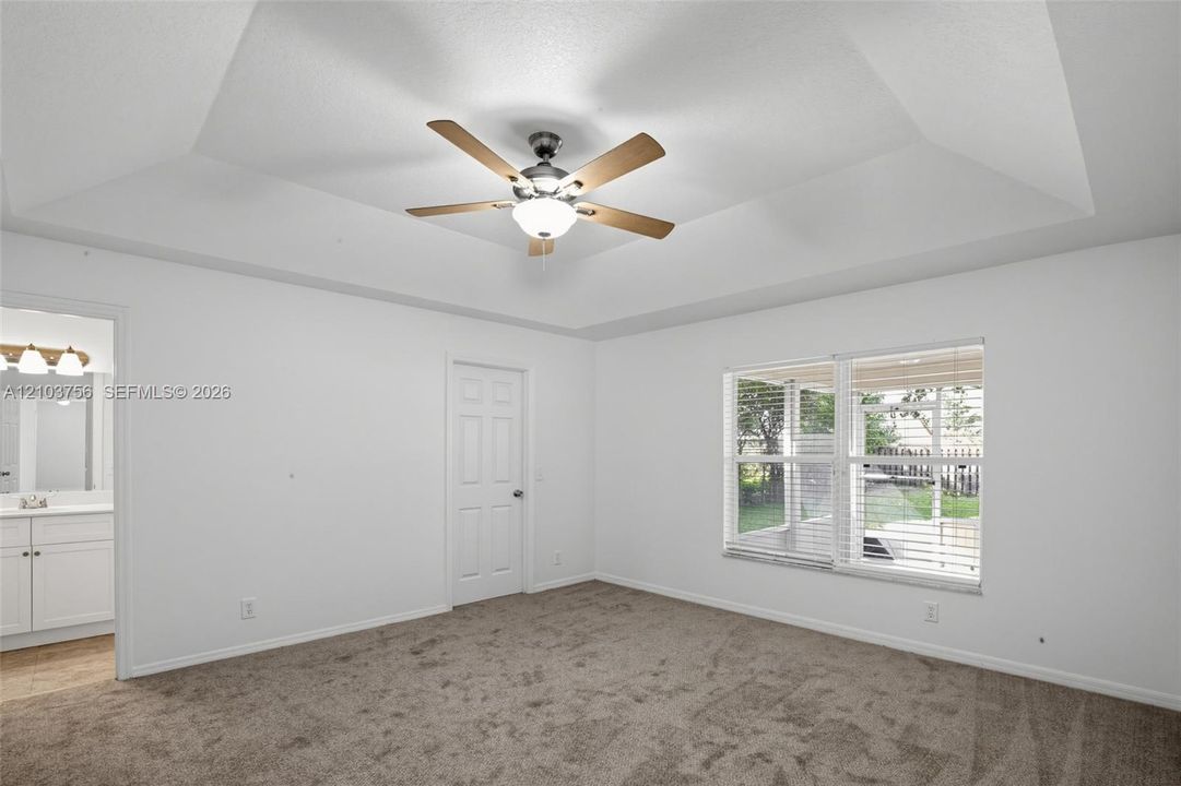 Tray ceiling with a central ceiling fan, carpeted flooring, and multi-pane window with blinds