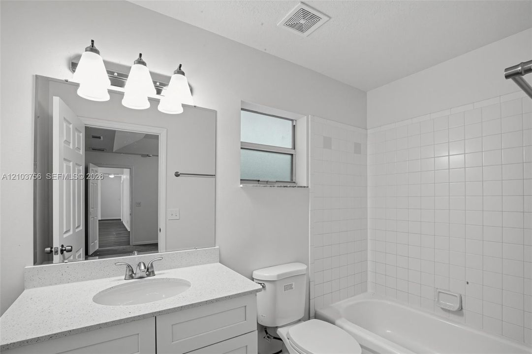 Bathroom featuring a vanity with a white countertop and oval under-mount sink, three-light fixture, wall-mounted mirror, and white tile tub surround