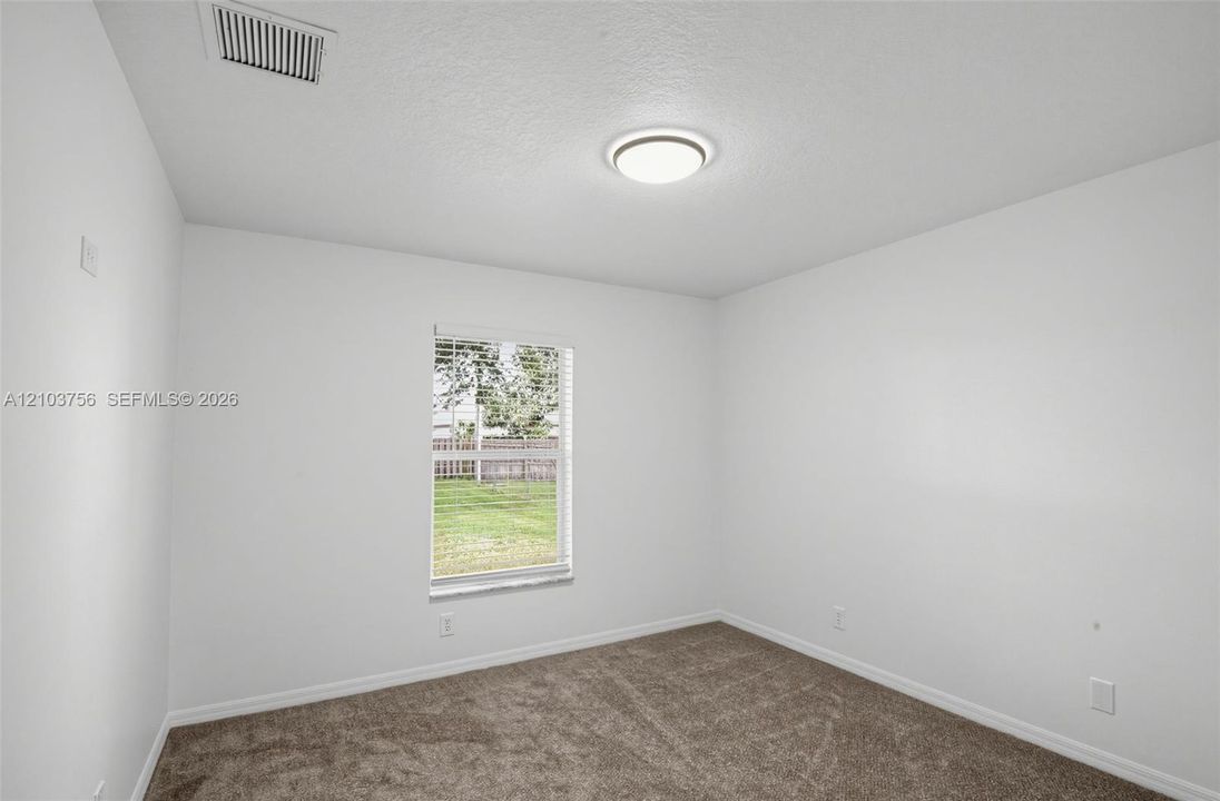 Neutral-toned carpeting, crisp white wall finish, flush-mount circular lighting fixture, and a single-pane window with horizontal blinds