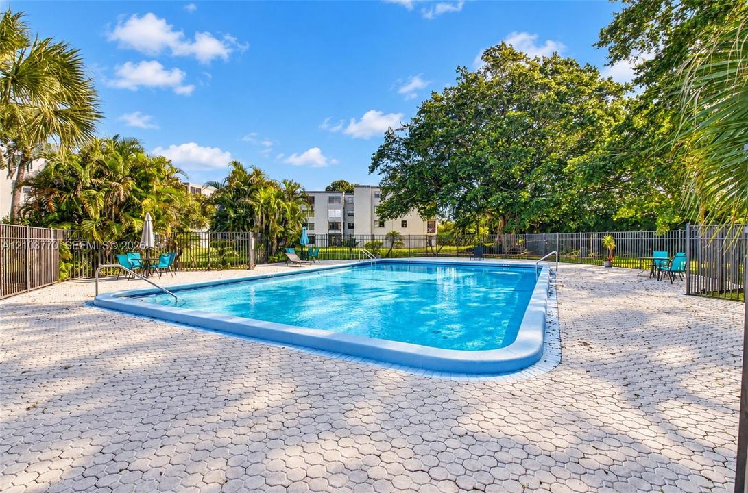 Rectangular swimming pool with a blue tiled border, surrounded by interlocking paver decking and a black metal fence