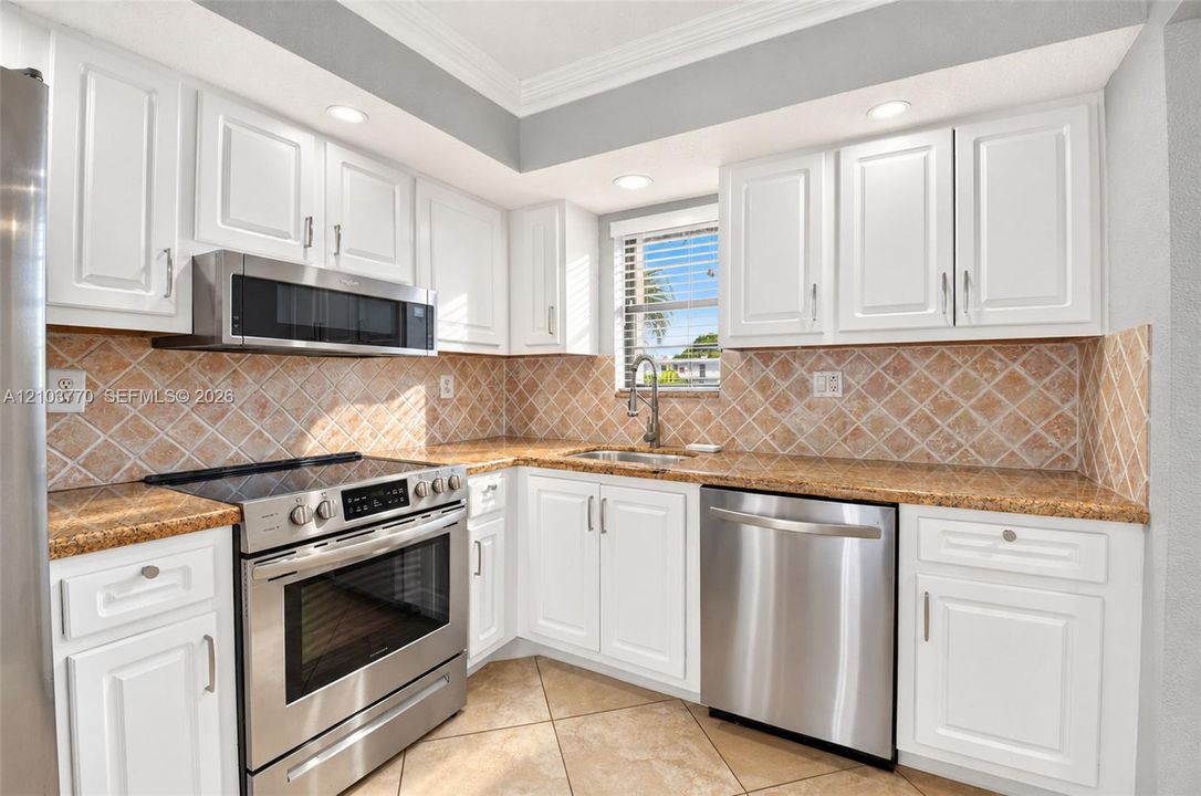 Updated kitchen featuring white shaker-style cabinetry, stainless steel appliances, granite countertops, and a full tile backsplash