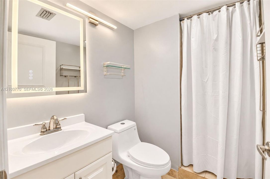 Illuminated mirror with integrated lighting, single vanity with a white countertop and basin, chrome-finish faucet, and a toilet with a white tank and bowl