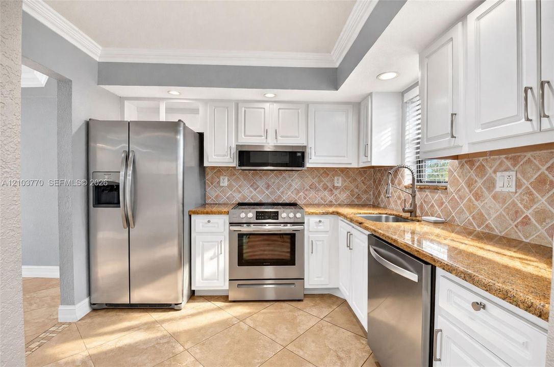 Kitchen featuring white cabinetry, stainless steel appliances, granite countertops, and a tiled backsplash