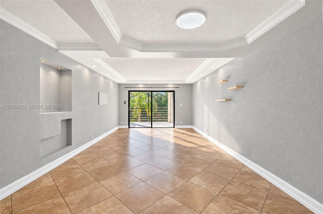Recessed ceiling with crown molding, tile flooring, built-in wall niche with lighting, and sliding glass door to exterior