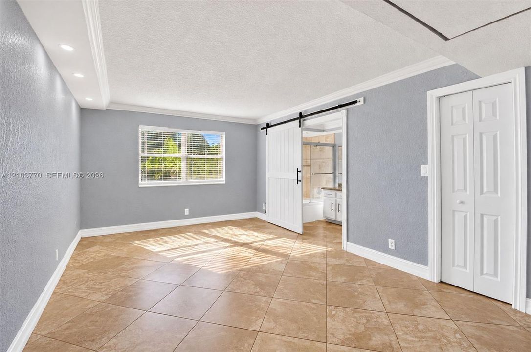Tiled flooring, window with blinds, recessed lighting, white barn door, and bi-fold closet doors