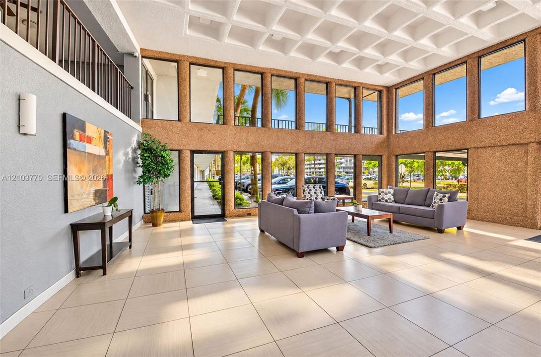 Spacious common area featuring a coffered ceiling, two-story window walls, ceramic tile flooring, and a second-story interior balcony with an iron railing