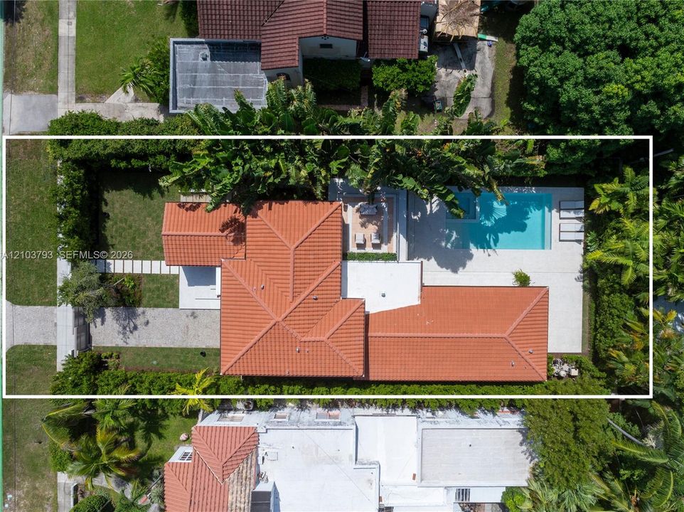 Aerial view of residential property featuring a clay tile roof, a rectangular swimming pool, a concrete patio, and mature perimeter landscaping