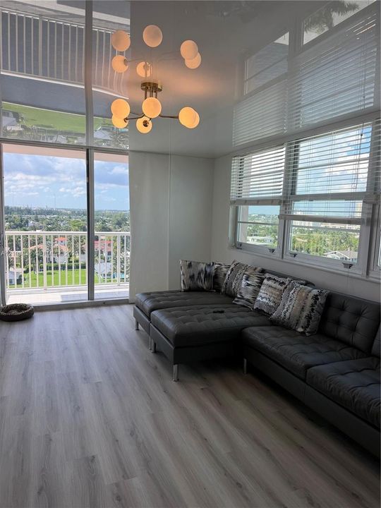 Spacious living area featuring wood-finish flooring, ample natural light from large windows, and a modern multi-bulb ceiling fixture