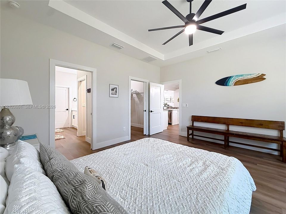 Tray ceiling featuring a multi-blade matte black ceiling fan, complemented by wood-finish flooring and solid-core interior doors
