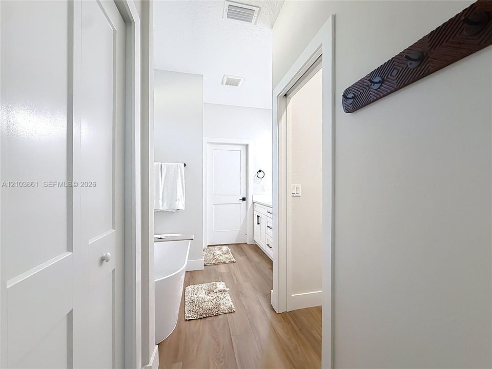 Bathroom featuring a freestanding soaking tub, white shaker-style cabinetry with neutral countertops, wood-finish flooring, and multi-panel interior doors