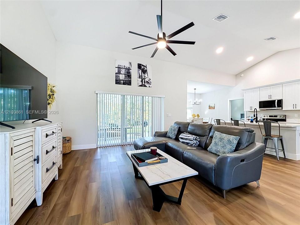 Living area featuring vaulted ceilings, wood-finish flooring, multi-blade ceiling fan, and sliding glass doors